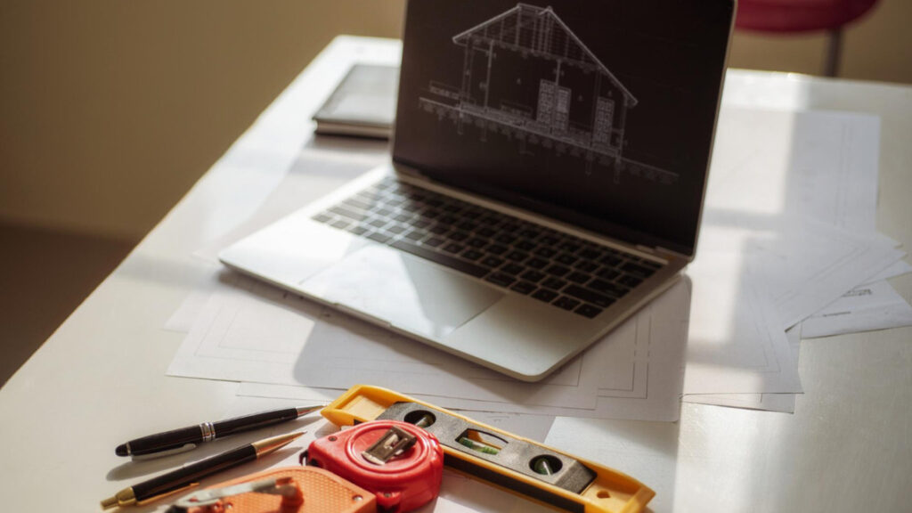 Laptop with roof blueprint and tools illustrating strategic website design for a roofing company in South Carolina